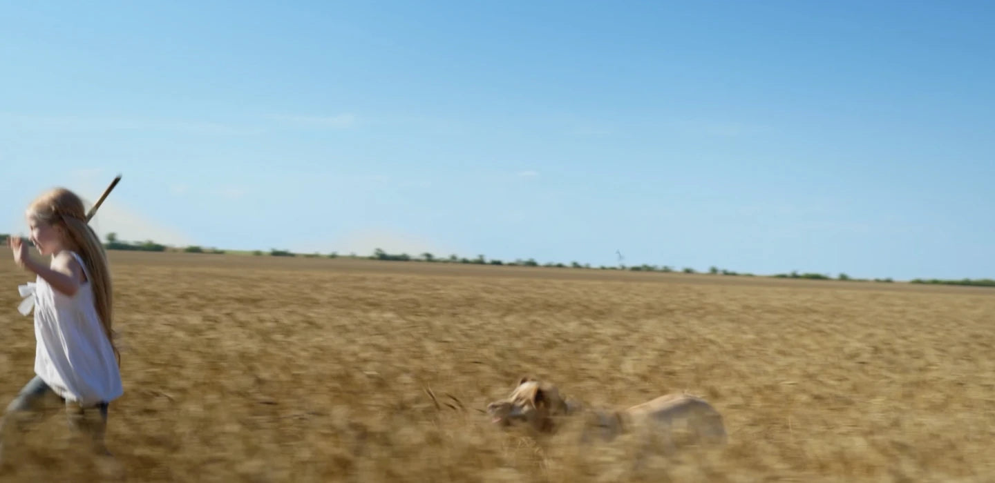 A young girl running through a wheat field with her dog right behind her.